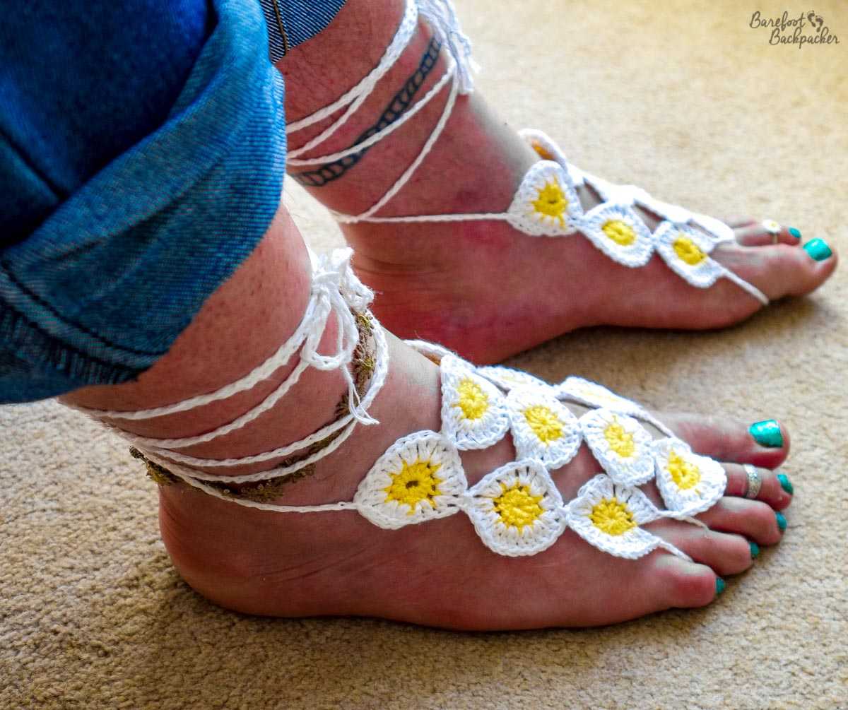 New barefoot sandals. White string/cord attached around my big toes and the toe next to the little toe, and tied around my ankles. Between them are 10 daisies, decorated in white and yellow crochet thread.
