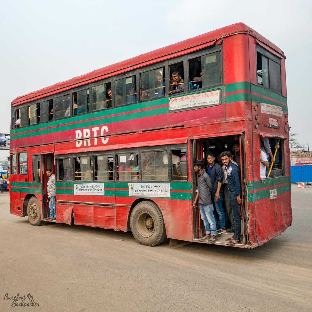 A typical bus in Dhaka – it's a red double-decker, it looks pretty old, and it's completely full to the extent that there are people just standing at the open door at the rear. They are not waiting to get off.