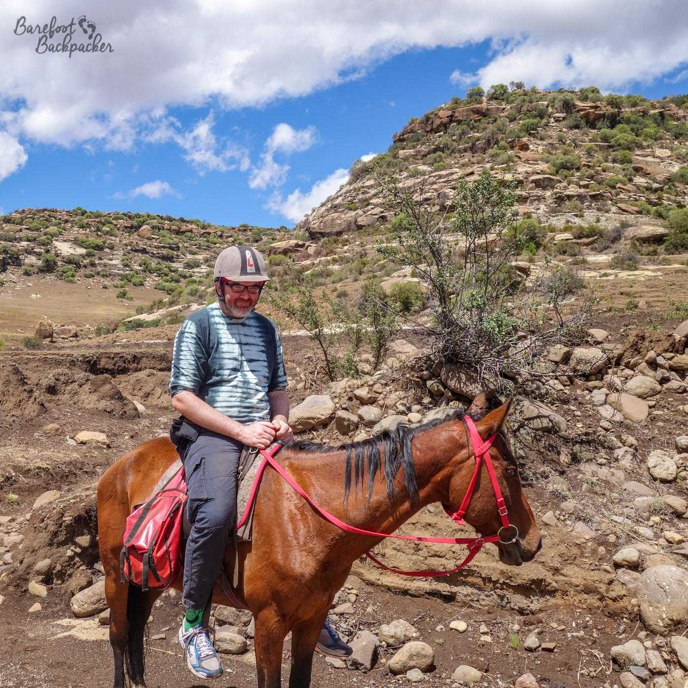 The Barefoot Backpacker, not barefoot, doesn't look entirely comfortable on top of a pony in the Lesotho rocky scenery. He is not a cowboy.