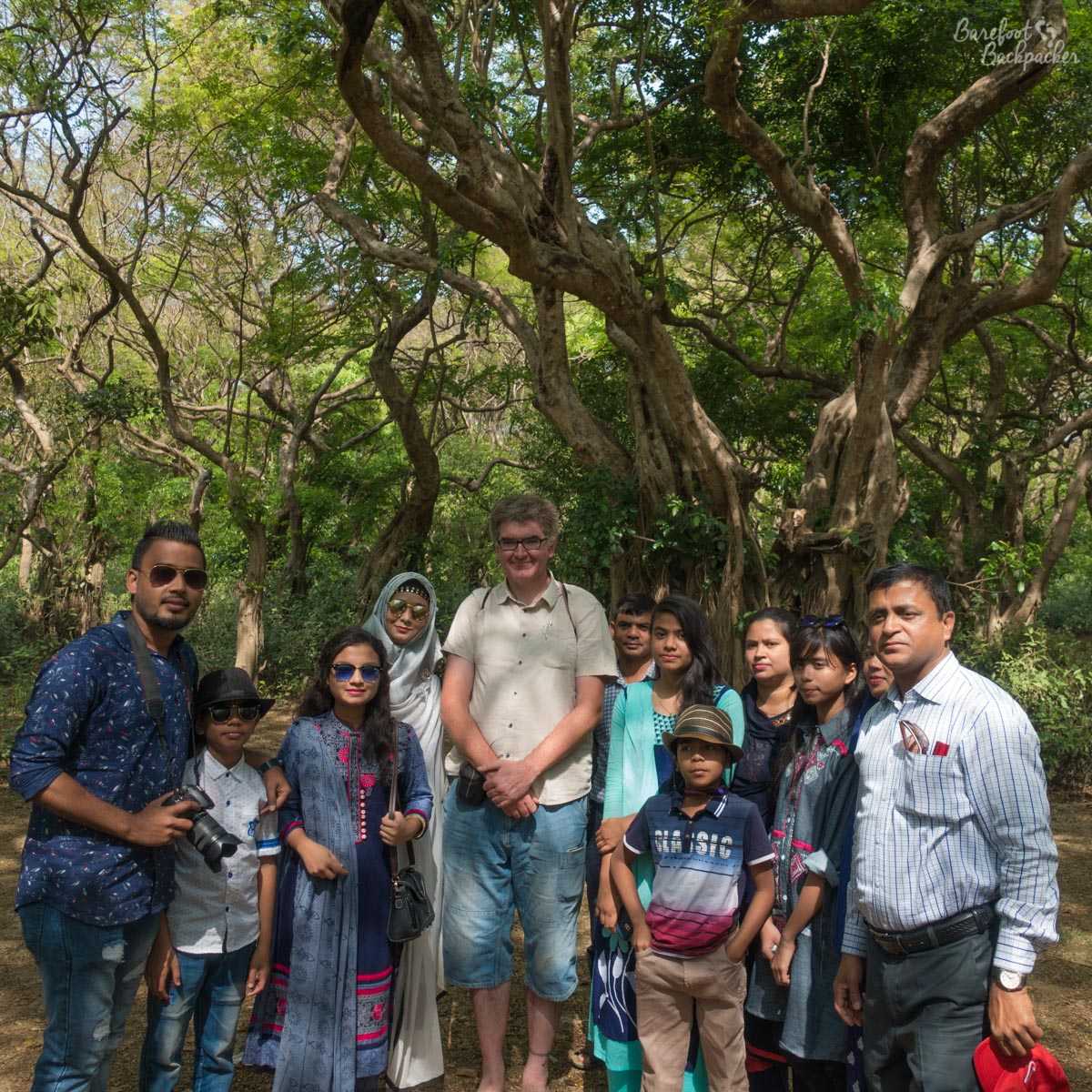 Several people stand in front of the camera with trees behind. I am in that group too, looking slightly awkward as I'm clearly out of place amongst a large Bangladeshi family.