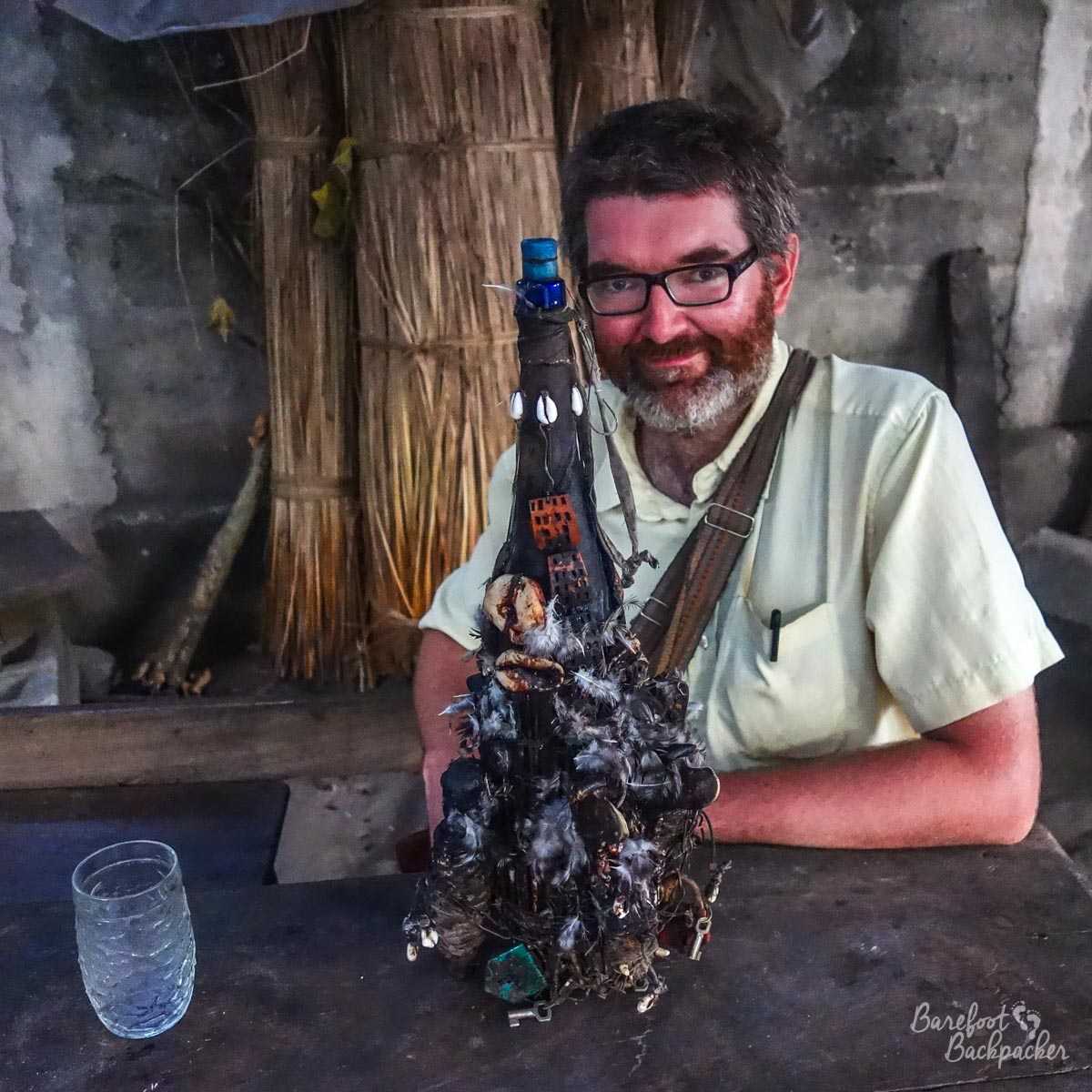 The Barefoot Backpacker is sat behind a table. On the table is a very ornately decorated bottle, with feathers, attachments, string, lots of stuff. What is in the bottle is something known only to the Vodun priest. But you can bet your life it won't be lemonade.