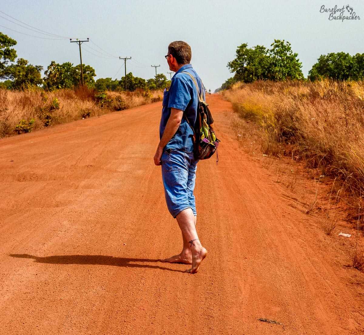 Standing barefoot on an orange gravel road in Ghana, West Africa. The road is lined with small trees but otherwise there is flat nothing. Pic taken, btw, by my moto-driver at the time.