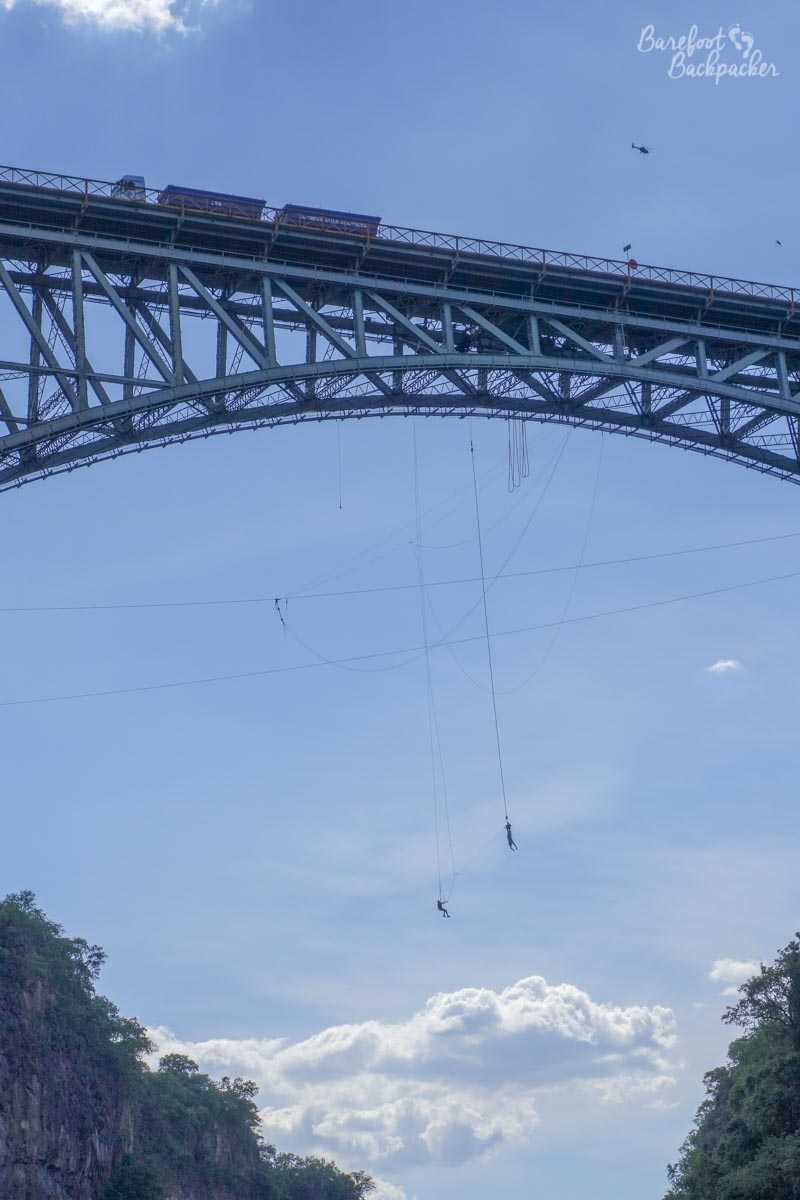 A couple of people bungee jumping from Victoria Falls bridge, with a clear blue sky behind them