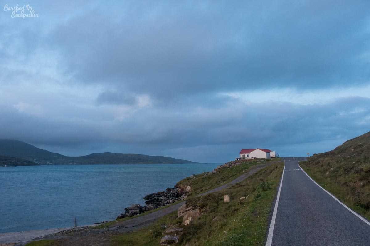 A lonely house by the side of the road and next to the sea on the island of Vatersay, at dusk.