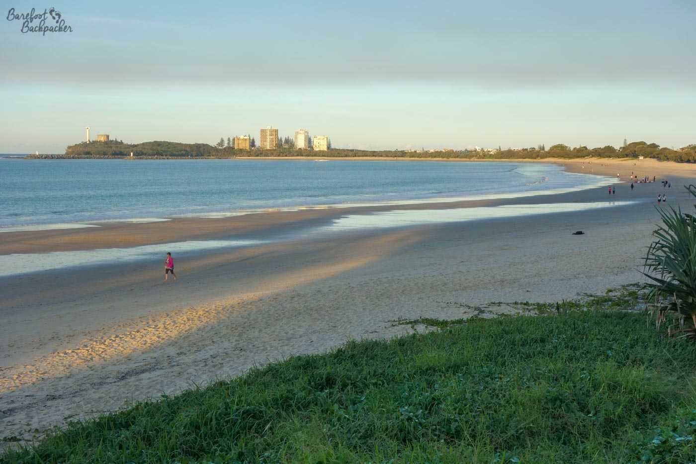 Mooloolaba beach. A wide curvy bay, which curls round to the left to end at a spit in the middle of the background. There's a couple of people on said beach, but otherwise it's sand and sea. Because it's a beach.
