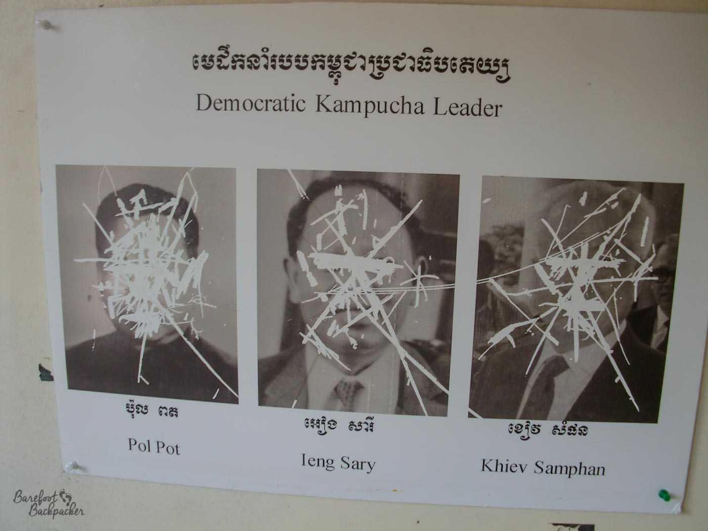 Photos of three of the 'Democratic Kampucha Leader', as it says: Pol Pot, Ieng Sary, and Khiev Samphan. Their faces have been nearly obliterated with scratches.