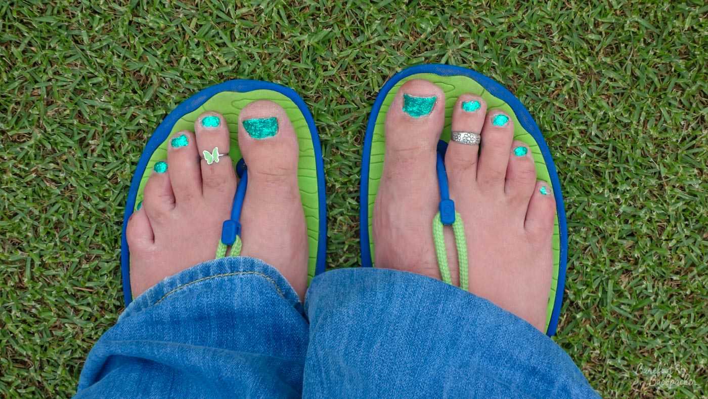 My feet in minimalist sandals, taken in Australia. The rubber upper sole of the sandal is lime green, on a blue under-base. These sandals have a blue piece of plastic between the toes, and a green cord is attached to them which fixes onto the back of the sandal, which you can't see because my jeans are in the way.