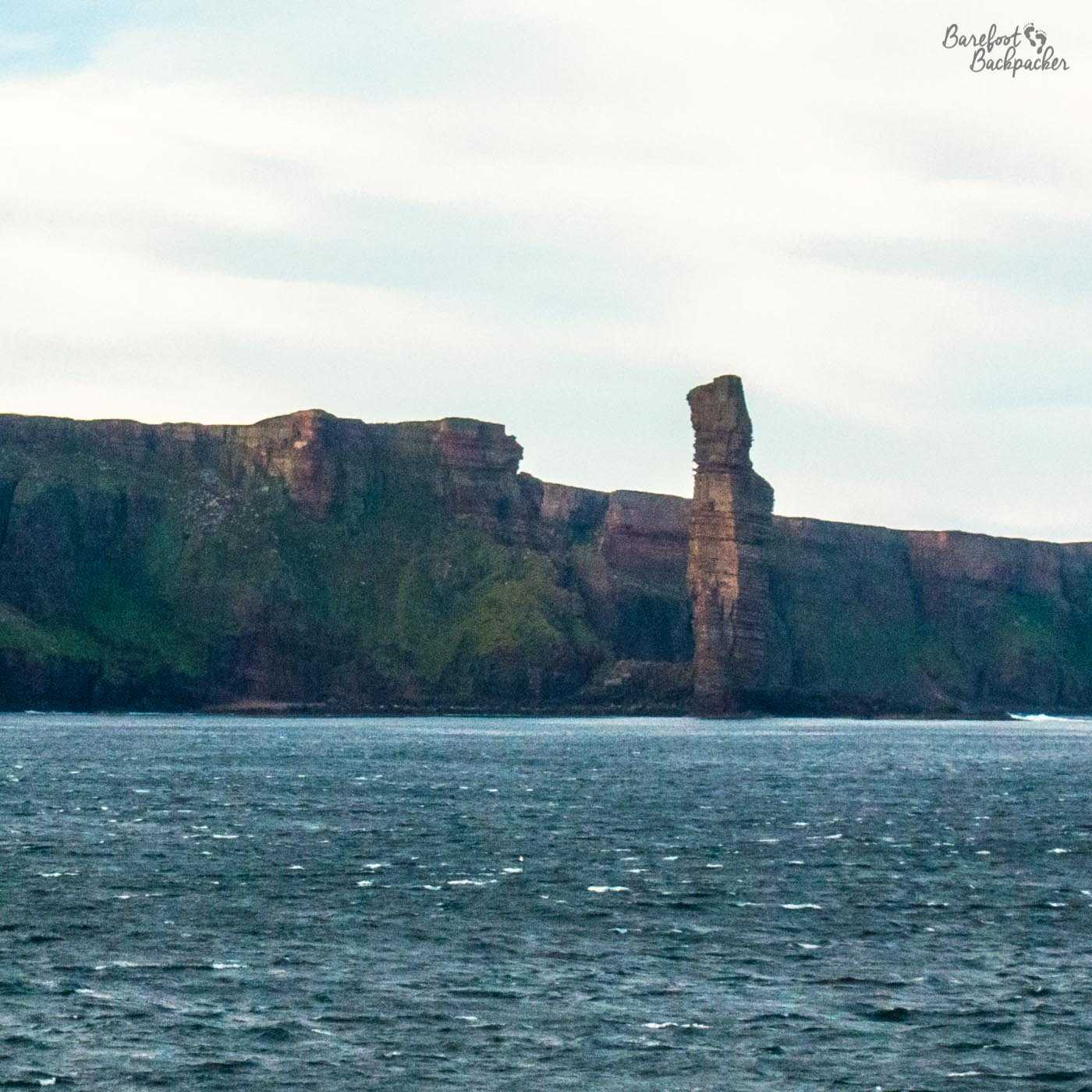 The Old Man Of Hoy, a rock stack off the coast of the island of Hoy, as seen from a passing ferry. It's taken from a distance, in the slightly less-than-optimal morning windy light, but you could make out its size (taller than the cliffs behind it) and its shape (a bit like a raised thumb).