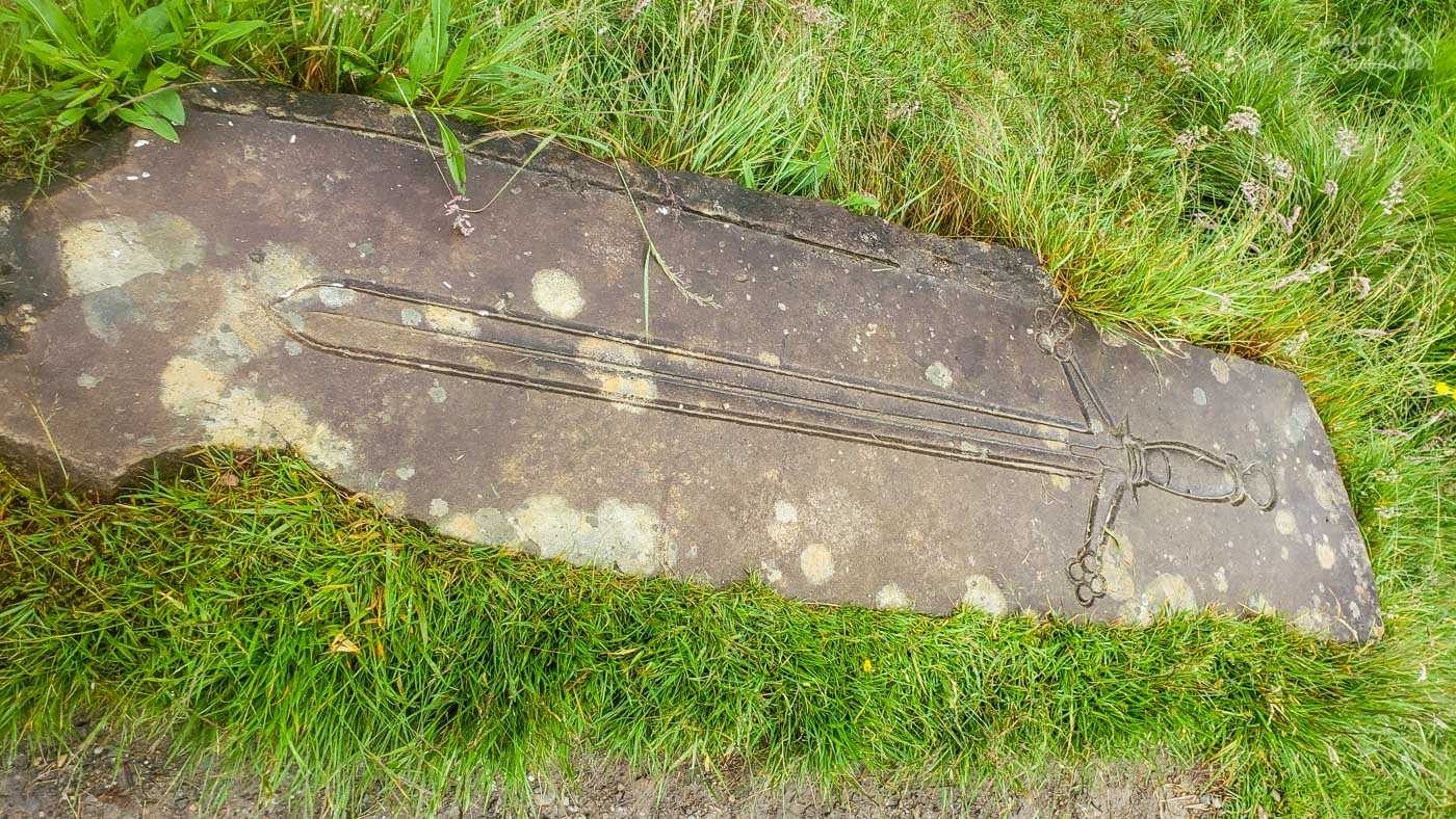The area around the site of the Battle of Dalrigh has a number of informational boards and stone etchings of facts and various concepts. This is a long stone with a representation of Robert The Bruce's sword. It has a small hilt, a handle that's slightly at an angle both sides, and a long blade.