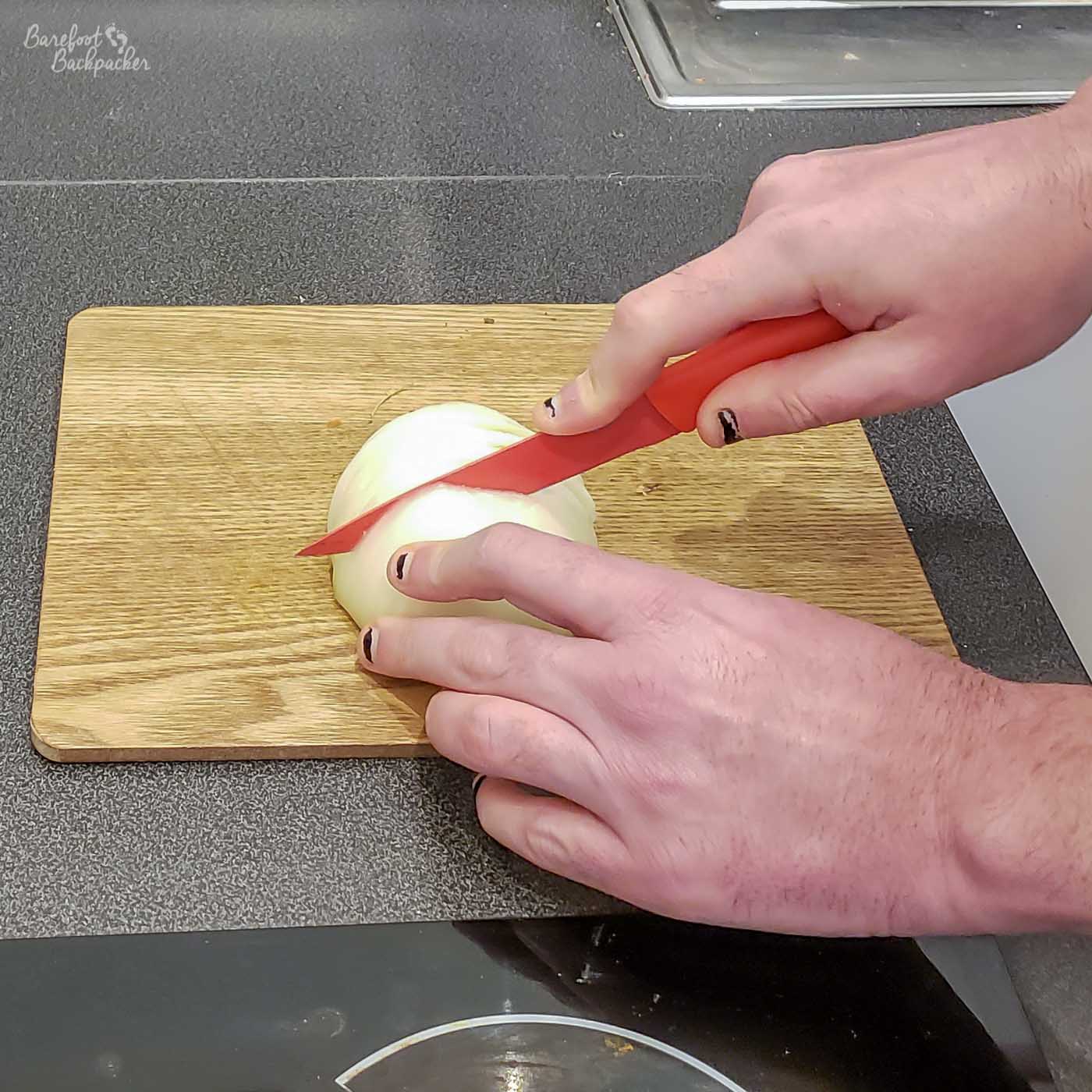Two hands, a red knife, a chopping board, an onion, no blood.