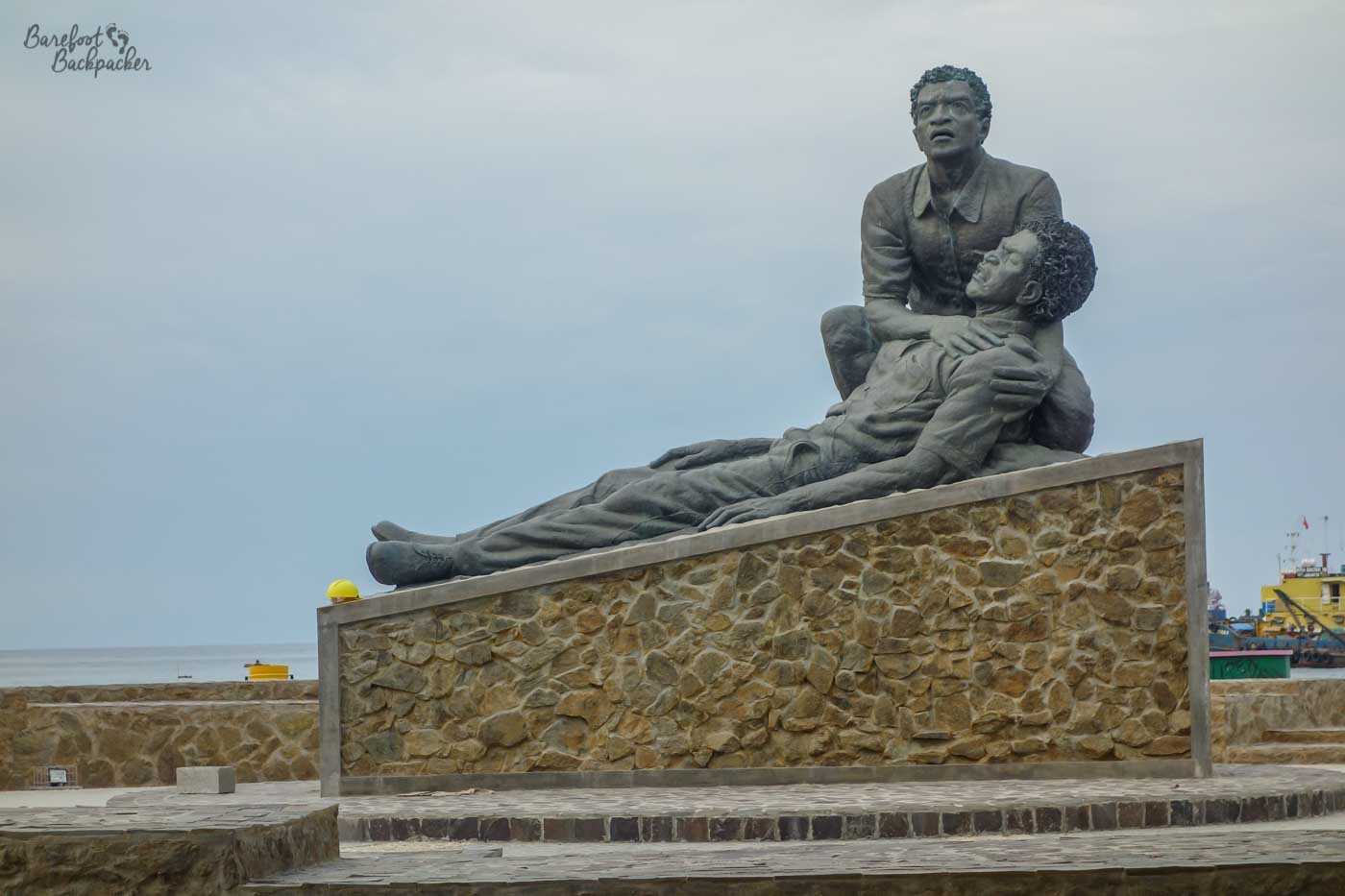 On a stone plinth is a statue of two men. One is lying down, presumably dying. The other is crouched behind them, cradling the dying man's head in their hands, and looking sadly out into the distance.