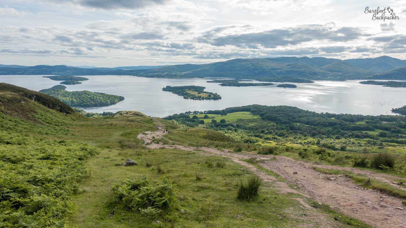 View from the top of a hill; grassy landscape and a large loch – body of water – in the midground.