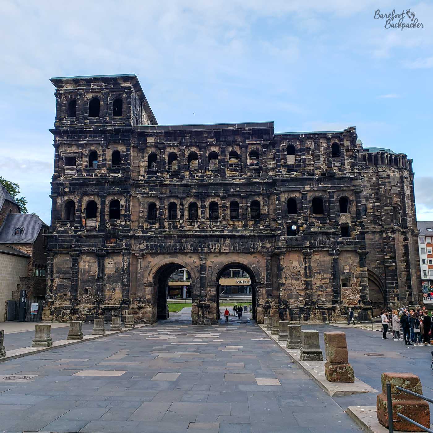 The remains of a large Roman stone gate / portal on the north side of the German city of Trier. It has four layers; at the bottom are two archways where the pedestrianised road passed through. Three bricked-up archways are set on either side. On the next two layers above, there is a horizontal line of small arched windows – 3 on either side and 5 on the main bit above the road. The bits on either side were towers, but the fourth and top layer only still exists on the left side. It has three more small arched windows and a square top. The road is lined on either side with small pillar bases.