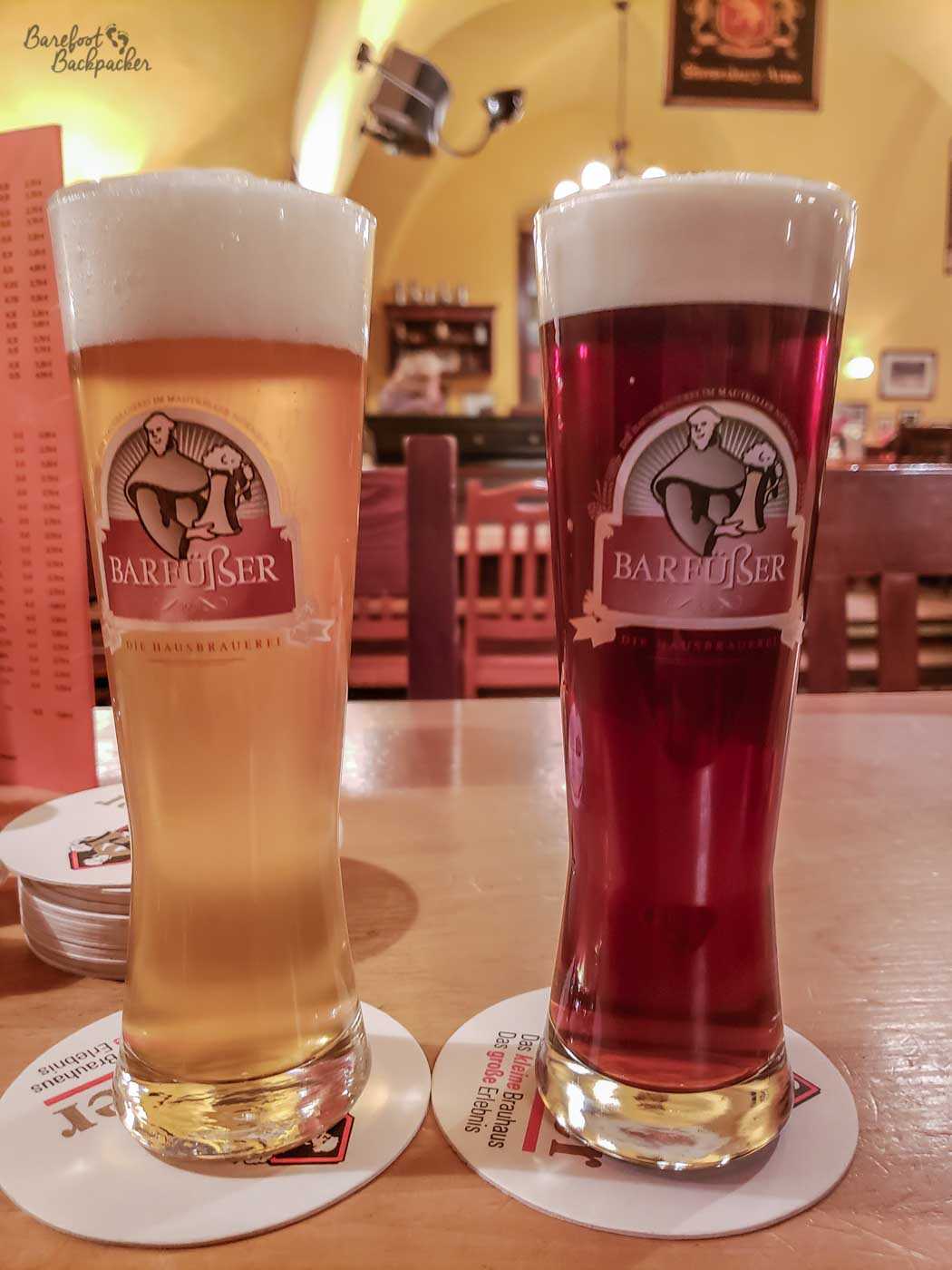 Inside the barfusser brewpub, Nuremberg. There are two branded glasses on the table, etched with an image of a monk – the one on the left has a blonde beer, the one on the right has a darker, more red-looking beer.