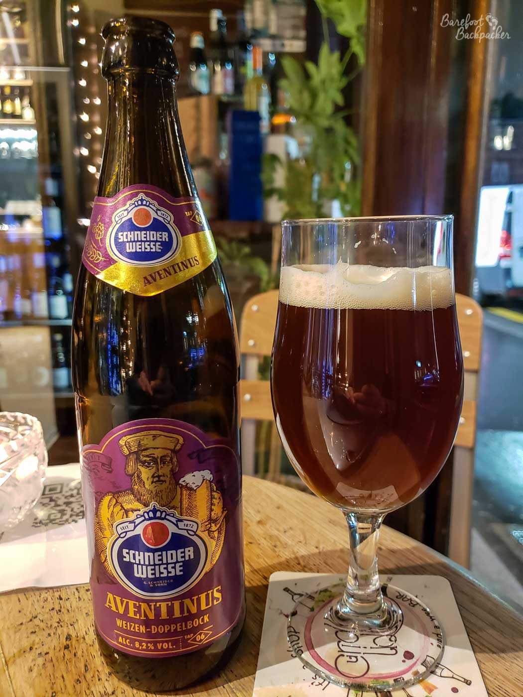 A bottle of beer stands on a table. To the right of it is a glass with the beer in. The beer is 'Schneider Weisse Aventinus'. It is a weizen-doppelbock and is 8.2%.