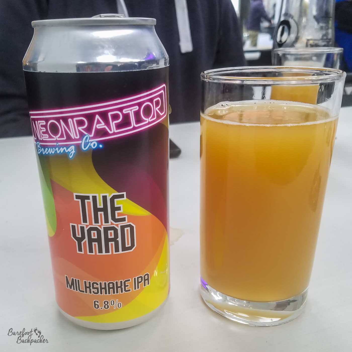 A can of 'The Yard', a beer from Neon Raptor, is on a table with a glass full of it next to it. The beer is cloudy and has the look and feel of a thick pulpy fruit juice. The style is known as a Milkshake IPA and it is 6.8%.