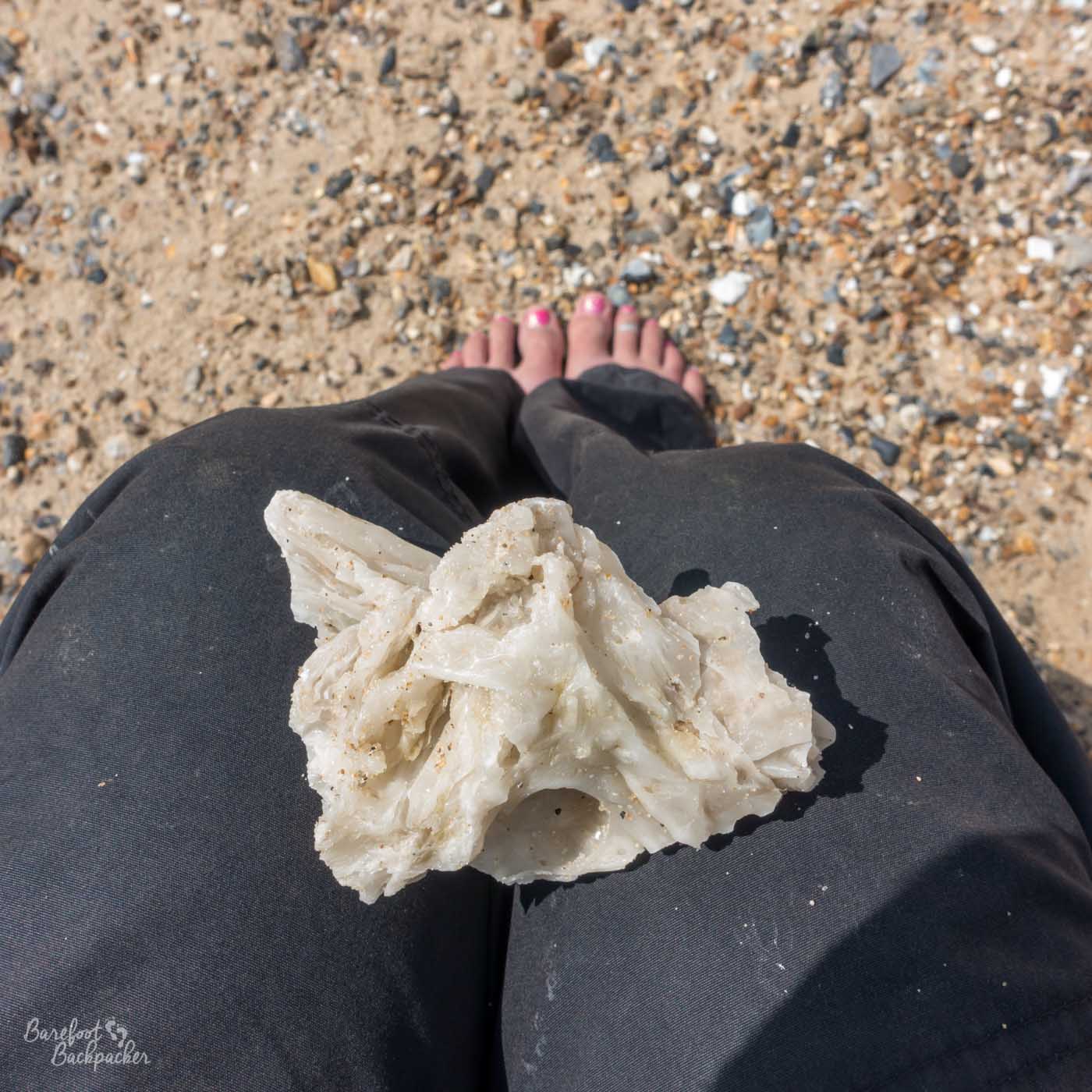 On a shingley beach, I'm sat down. The camera is pointed at my trouser-covered lap, on which is a lump of palm oil - an irregular shape with jagged edges, about the size of my hand.
