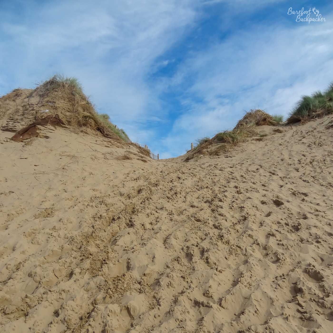 Formby Nature Reserve; a wide sand trail covered in footprints goes up between two dunes, away from the beach.