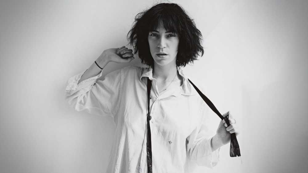 Image of rock icon Patti Smith, black/white. She's wearing a shirt and wielding a tie, either putting it on or taking it off.