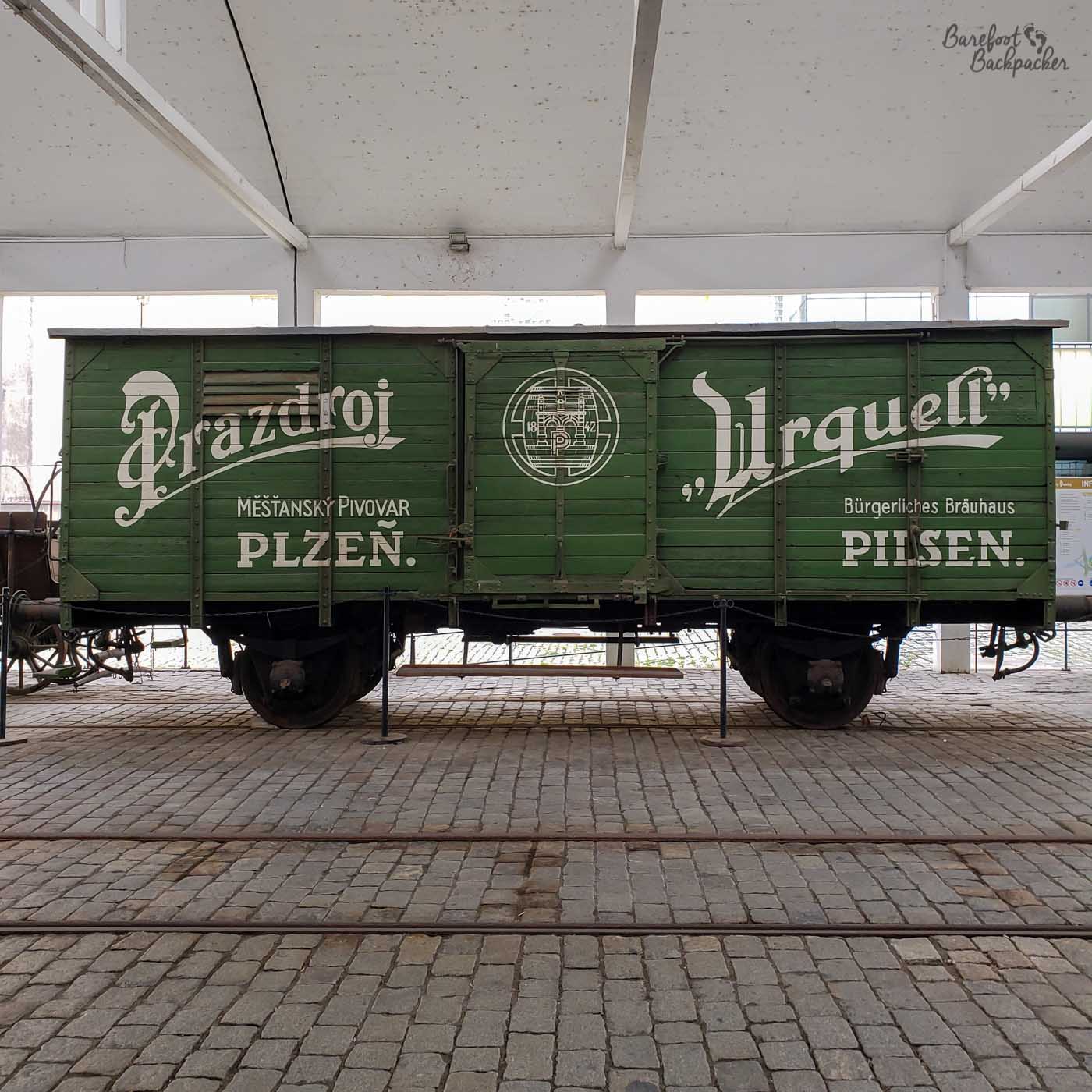 An old rail wagon – rectangular and open-roofed. On the side is an advert for, and logo of, Pilsner Urquell.