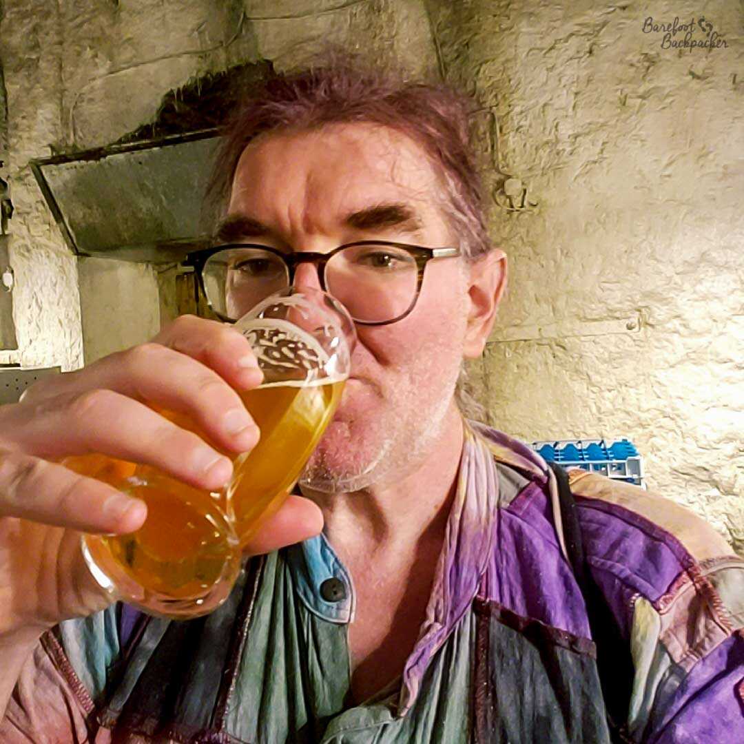 A person sits in a cavern, drinking a glass of Pilsner.