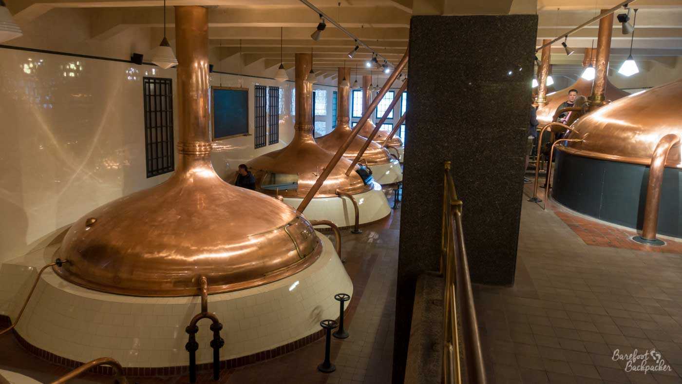 Large room on two levels, full of copper kettles. The bottom of them is circular and ceramic, on top of which is a circular brass lid, from which comes a tall copper chimney reaching through the ceiling. There's four on the lower level of the room and two on the upper level.
