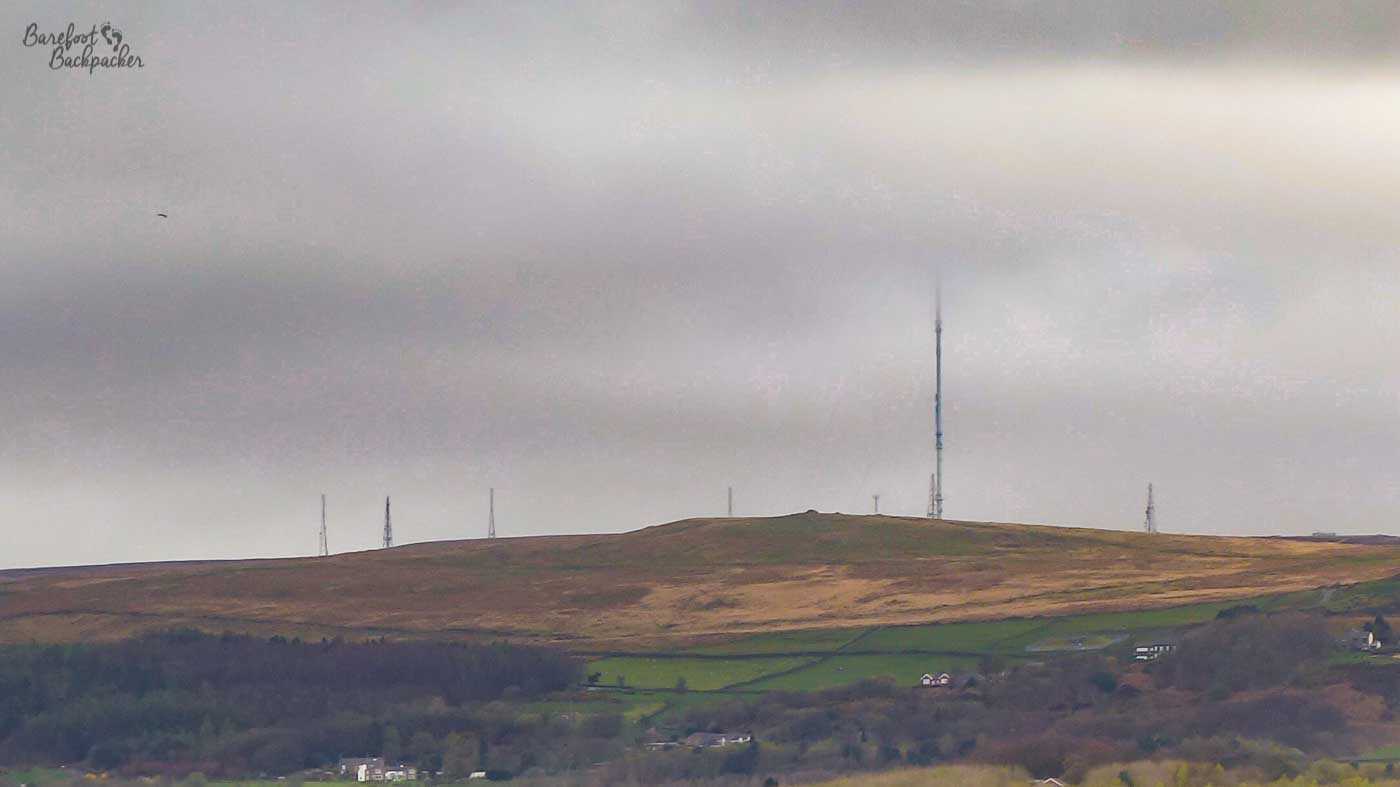 Image of a series of broadcast transmitters, one taller than the others, on a hill in the distance in the mist.