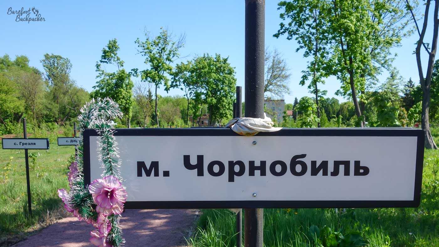 Close-up of a small sign that would tell you you're in Chernobyl City. It's one of many signs along both sides of a path, each on a pole. This one has a small wreath of flowers hanging off it.