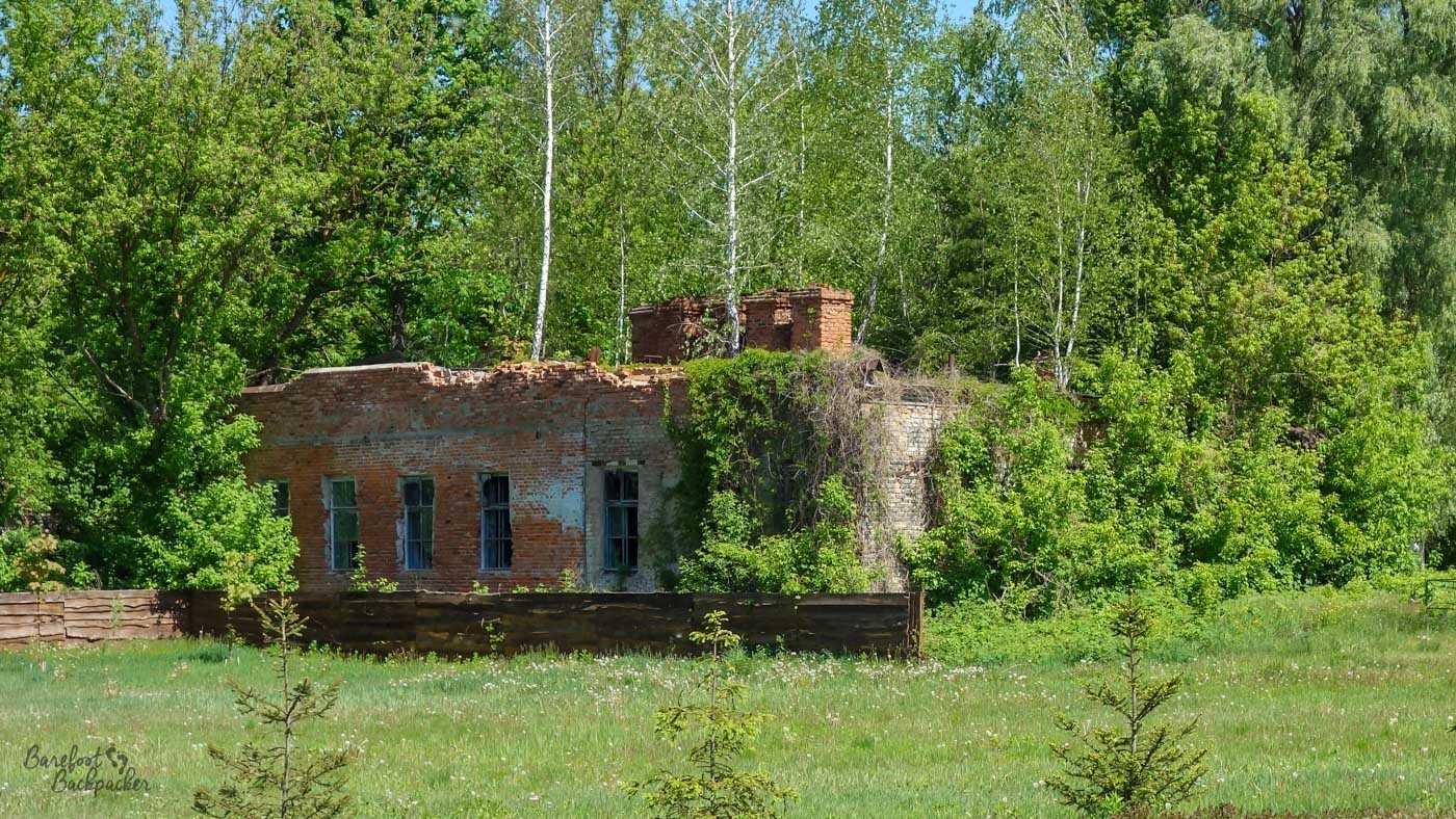 One of the ruined buildings in Chernobyl City; it's a brick rectangle with possibly no roof and some broken bricks at the eaves. There are trees growing through the walls. It lies some distance away on a lawn.