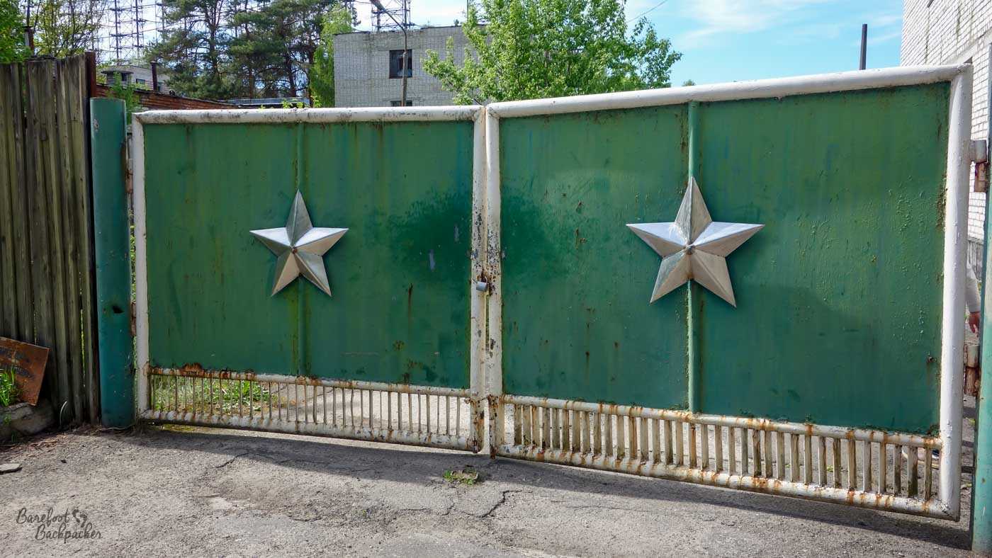 The entrance to the Duga Array. It's two solid gates in the road that open outwards from the middle. On each of the gates is a large embossed 5-pointed star. Just behind the gates the edge of the array can be seen.