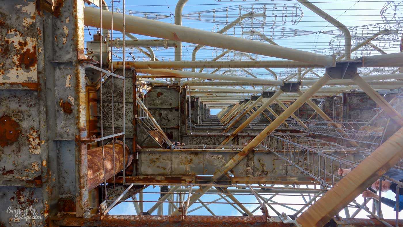 View from directly underneath the Duga Array frame, looking upwards. The pattern of the frame is such that a small patch of sky is visible between all the metallic pipework.