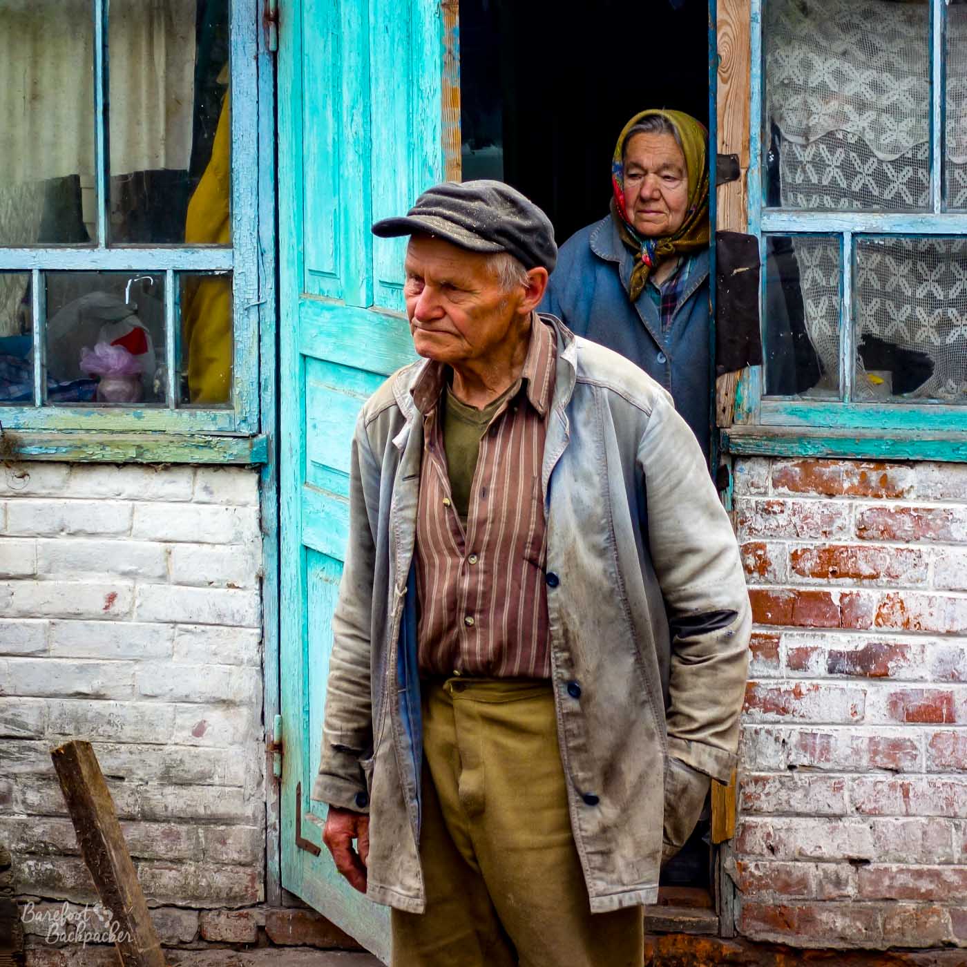 Two elderly people standing outside their cottage.