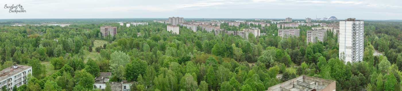 Panorama of Pripyat, taken from above. There are tower blocks visible, but they're just poking out above the canopy of trees, like a series of swimmers in the sea of green.