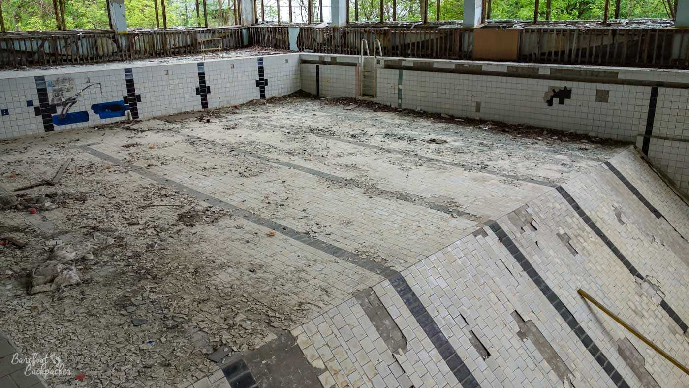 The empty swimming pool in Pripyat. The tiling is still mostly intact, and it's clear where the shallow end is as the floor is flat for a bit until a certain point where it sharply slopes downwards. The steps into the pool are still visible too.