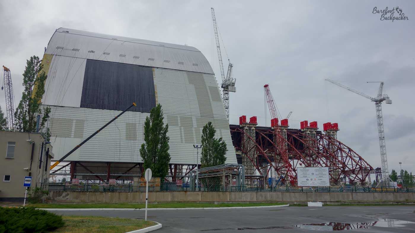 Fairly close-up view of the Chernobyl reactor taken from the service road. The new shield, a concrete armadillo-like structure, is being readied. There are cranes and metal frameworks in place to the right of it.