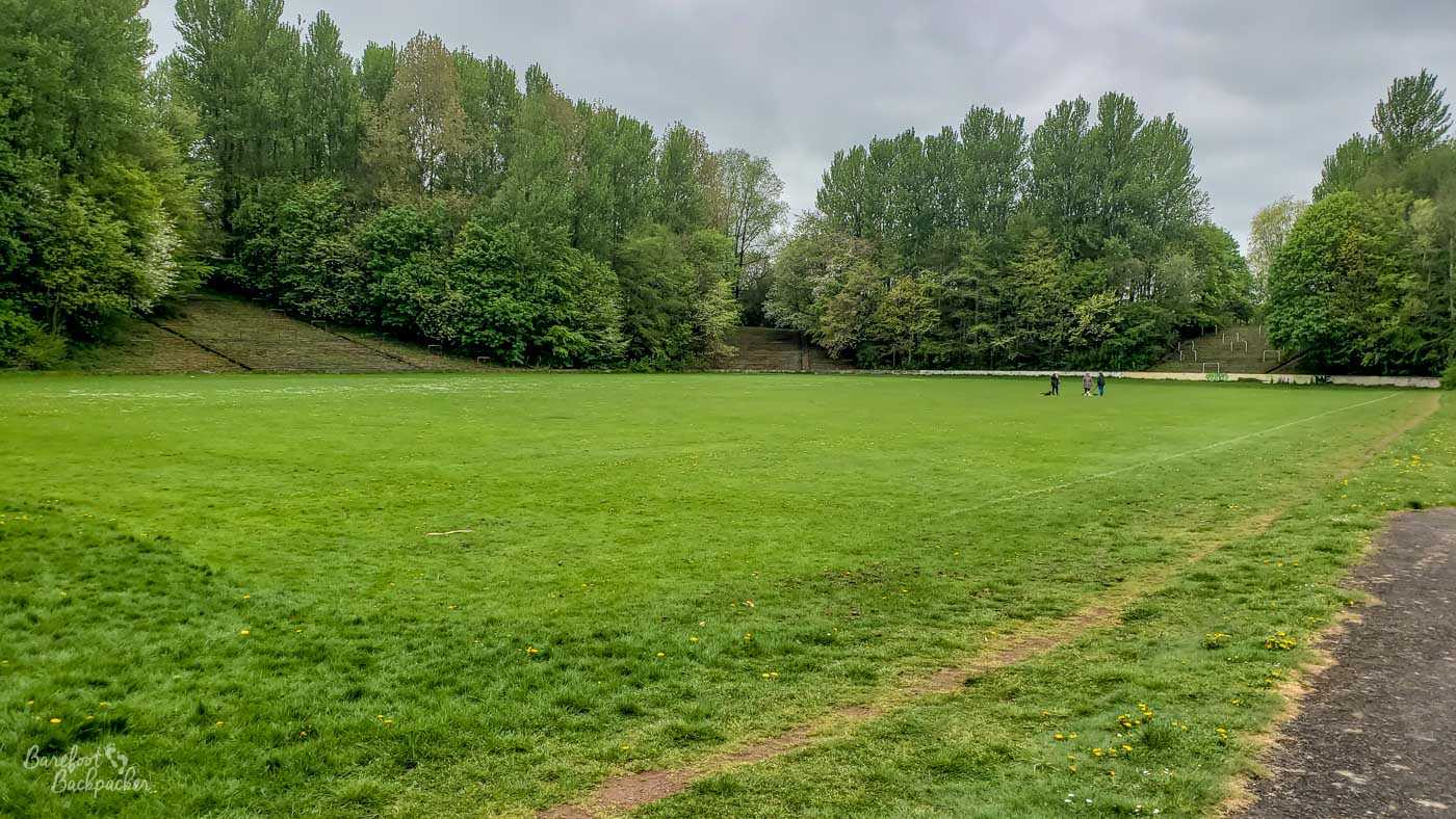A flat piece of lawn with faded pitch markings on it. Surrounding the pitch the land rises in banked structure, but trees block part of it so it'd be impossible to walk around the banking.