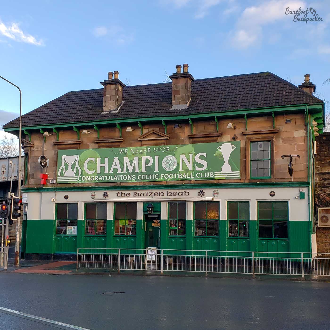 A long rectangular building, mostly painted green, with a large banner above the windows that congratulates Celtic Football Club for being Champions.