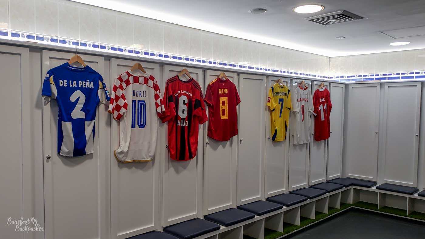 A plain dressing room, with football shirts on several of the lockers.