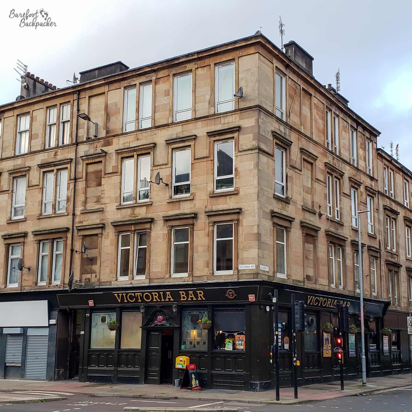 A four-storey tenement block with a pub at the ground level, called the Victoria, stands at a crossroads.