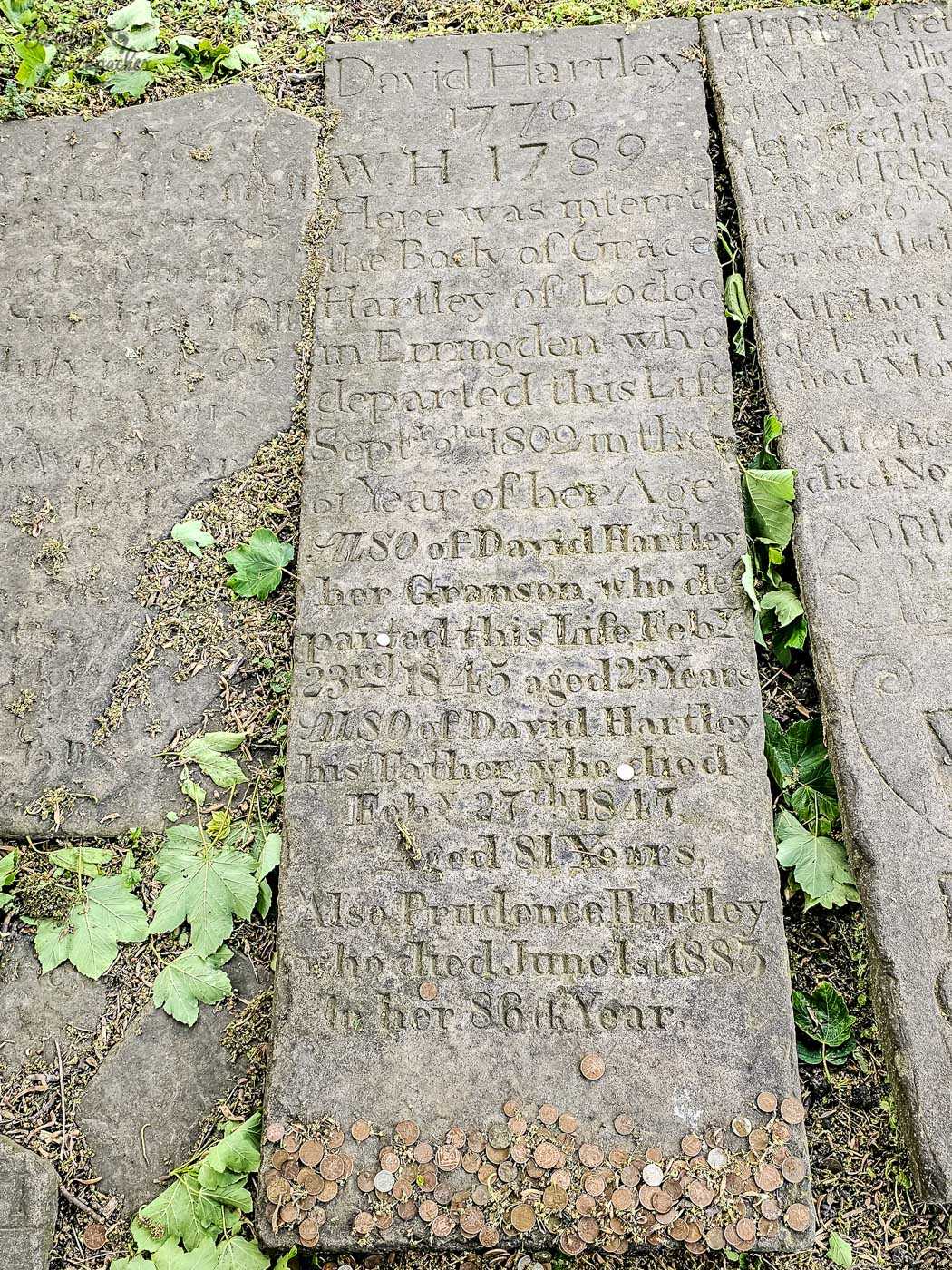 An eighteenth-century gravestone laid flat in the churchyard at Heptonstall, its weathered inscription still clearly visible with dozens of coins left along the bottom edge.