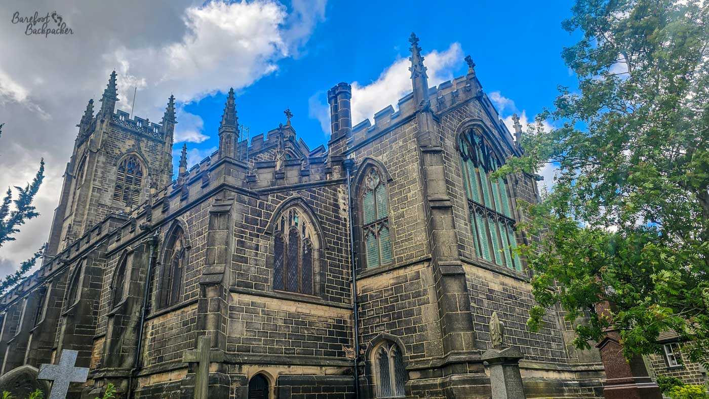 The Gothic parish church of St Thomas the Apostle in Heptonstall, viewed from the churchyard beneath a dramatic cloudy sky.