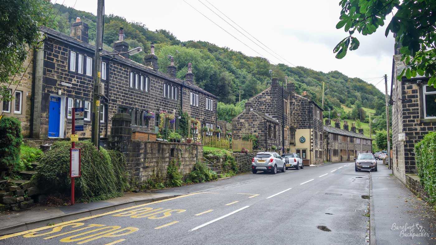 Stone houses lining the main road through Cragg Vale beneath wooded hillsides.