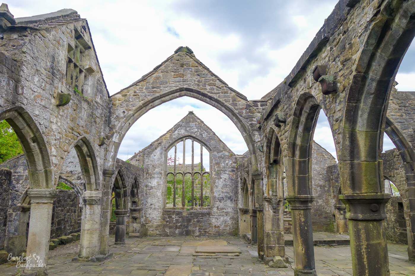 The roofless stone ruins of St Thomas Becket Church, with Gothic arches and window openings framing the open sky.