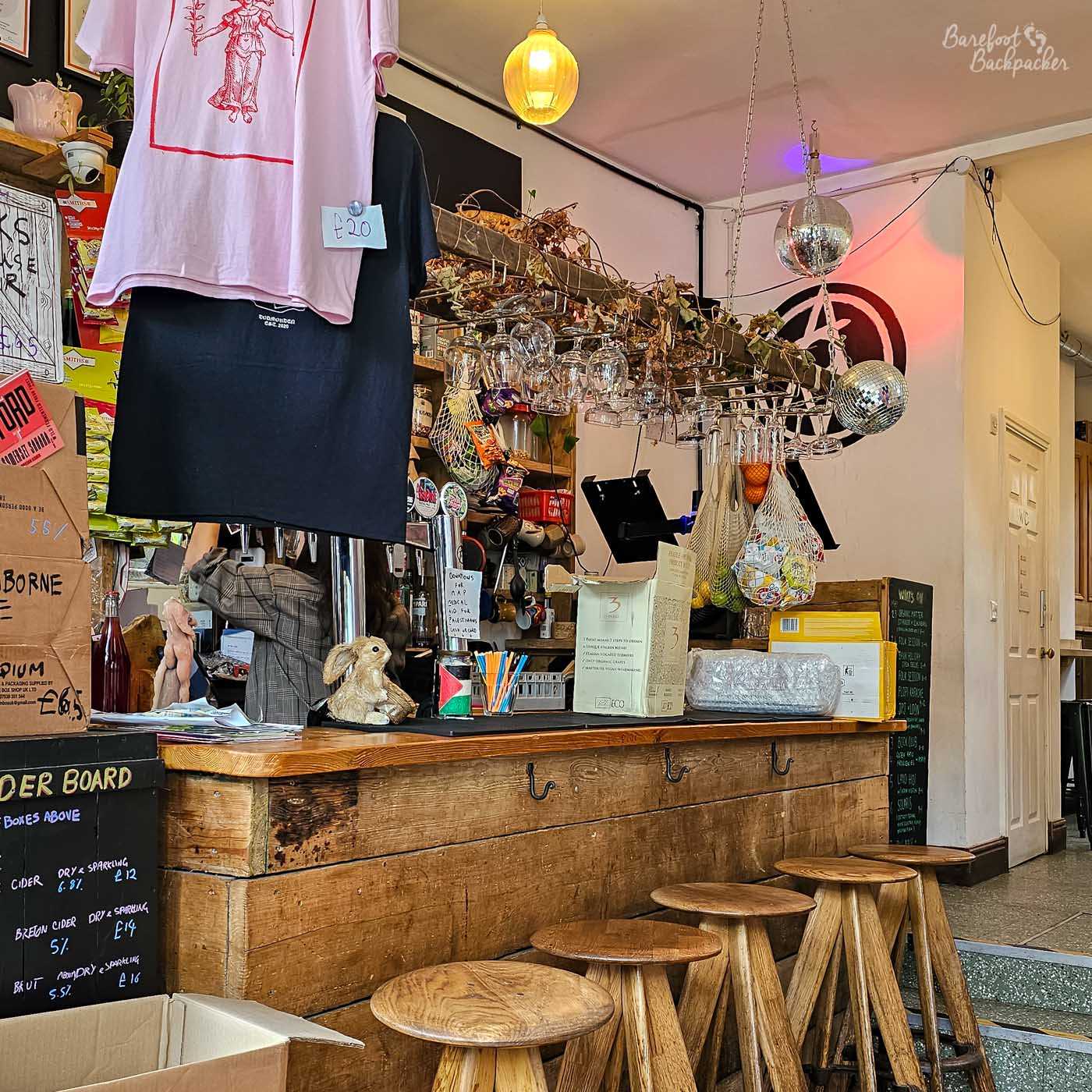 A rustic wooden bar dominates the centre of Nan Moor's, surrounded by mismatched stools, hanging wine glasses, merchandise and quirky decorations. Disco balls, dried foliage and bags of fruit hang above the counter, giving the small venue a creative, slightly unconventional feel that matches its independent character.