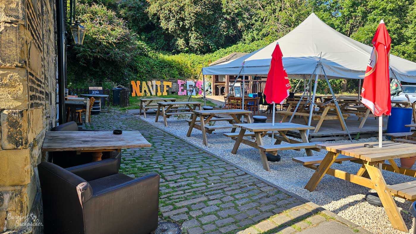Behind the pub, a spacious beer garden combines cobbled paths, gravel seating areas and rows of wooden picnic benches beneath large white canopies and red umbrellas. Colourful letters spelling